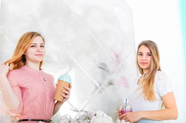 Dwie śliczne dziewczyny w sukienki pić napoje z filiżanek z pokrywkami i t - Zdjęcie, obraz