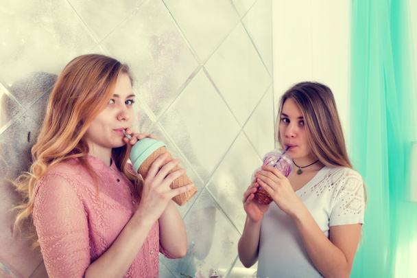 Two cute girls in dresses drink drinks from cups with lids and t - 写真・画像