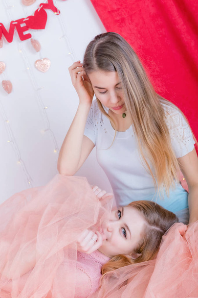 Two cute long-haired girlfriends in dresses sit and cuddle again - Photo, Image