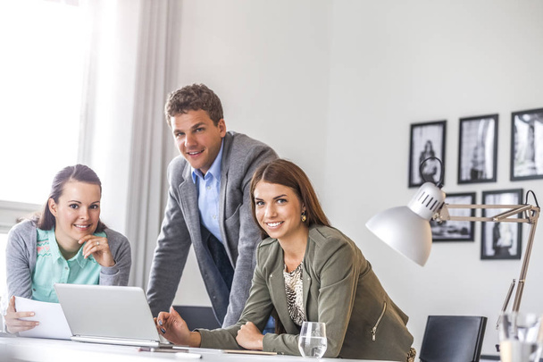 Portrait of smiling young businessman with female colleagues at desk in office - Photo, Image