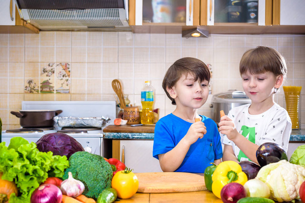 Healthy eating. Happy children prepares and eats vegetable salad in kitchen - 写真・画像