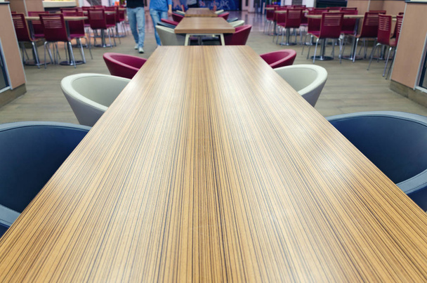 Vista superior de la mesa larga de madera de color amarillo-marrón con sillas azules y blancas. Detalles del interior de la cafetería en el centro comercial. Espacio de copia vacío para texto
. - Foto, Imagen