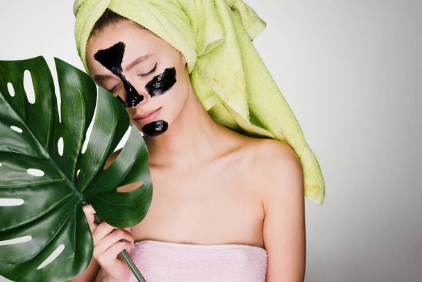 young girl with a green towel on her head enjoying a spa, under the eyes of black patches, holds a green leaf - Foto, Bild