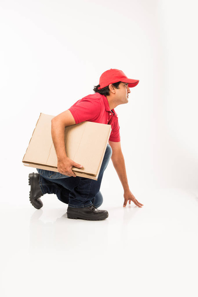 Delivery Concept - Portrait of Happy Indian or delivery man in red or green uniform walking or jumping or checking or presenting cardboard box with copy space - Photo, image