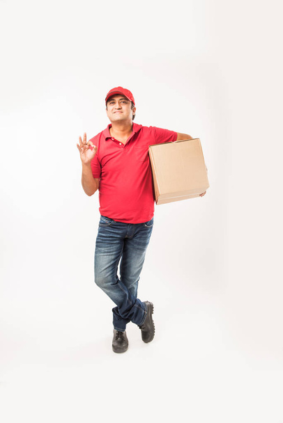 Delivery Concept - Portrait of Happy Indian or delivery man in red or green uniform walking or jumping or checking or presenting cardboard box with copy space - Zdjęcie, obraz
