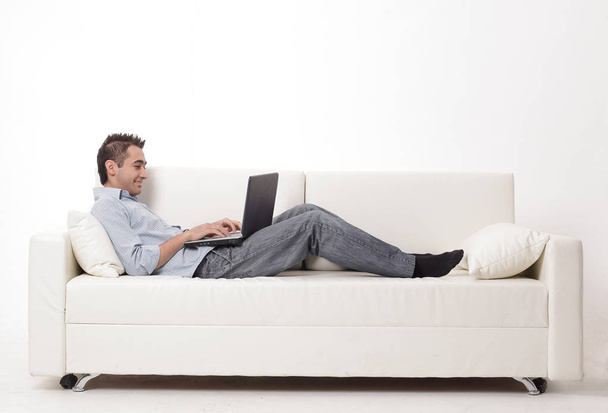 man working on laptop lying on a sofa - Foto, Imagen
