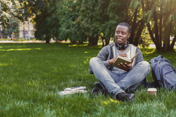 African-american student reading book in campus on grass - Fotoğraf, Görsel
