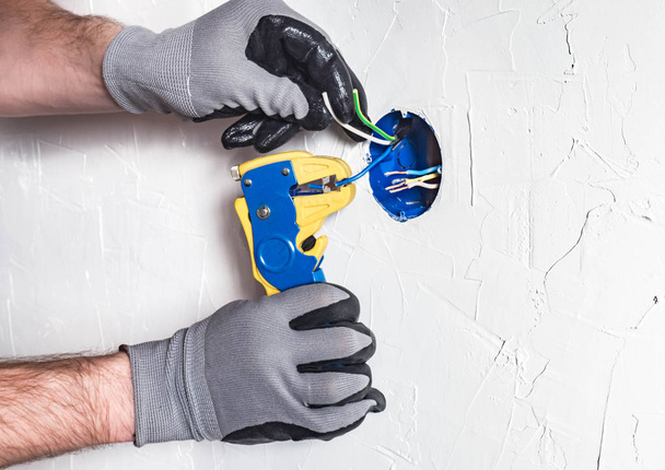 Le mani degli elettricisti con uno speciale utensile puliscono i fili in una scatola di giunzione
 - Foto, immagini