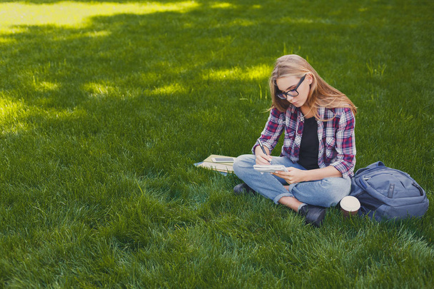 Молода жінка сидить з блокнотом на траві
 - Фото, зображення