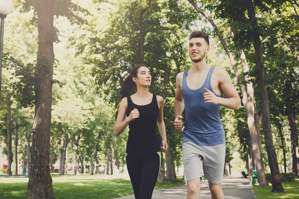 Jonge vrouw en man joggen in groen park, kopie ruimte - Foto, afbeelding