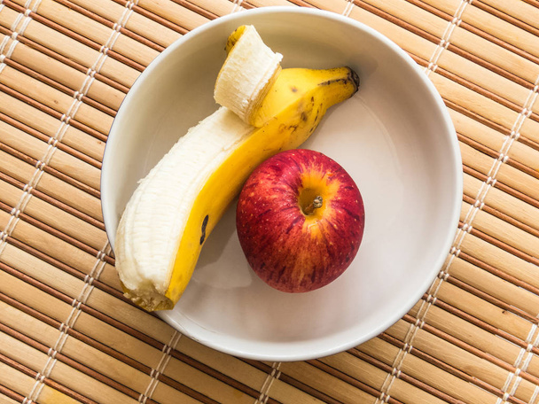 Banan i jabłko, wewnątrz białe miski, gotowy na lekki posiłek, na drewnianym stole. - Zdjęcie, obraz