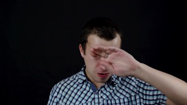 A crying wiping tearful young man on a black background in slow motion - Materiał filmowy, wideo