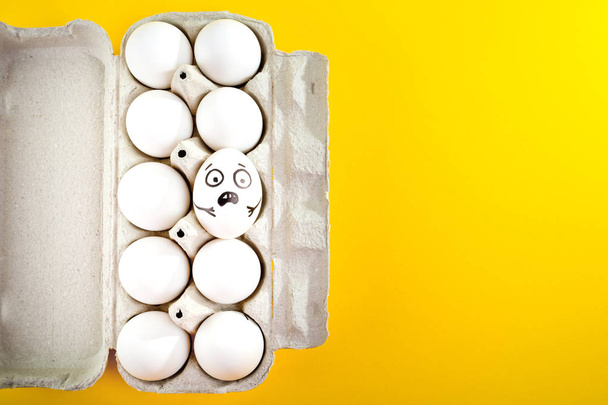Velikonoční vajíčko s legrační obličej v zásobníku na žlutém podkladu. - Fotografie, Obrázek