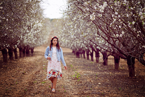 In spring, a young red-haired woman with a floral wreath and in a white dress running in a field on the grass - Foto, Imagen