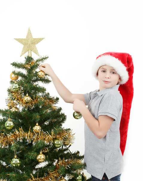 Menino com chapéu de Papai Noel decora a árvore de Natal
 - Foto, Imagem