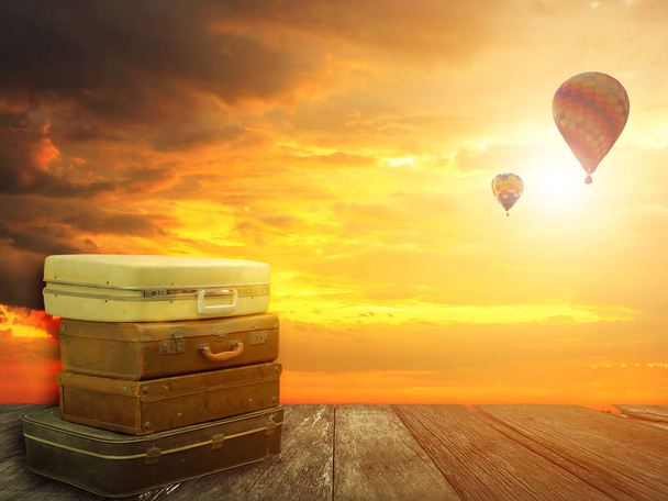 Halmozott bőr poggyász a fa deszka a hőlégballonok napnyugtakor ég háttér. Utazási koncepció. Legjobb út fantázia jellegű háttérrel. - Fotó, kép