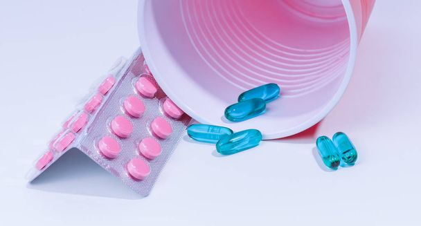 Зеленые и розовые таблетки и почти опрокинутый контейнер
 - Фото, изображение