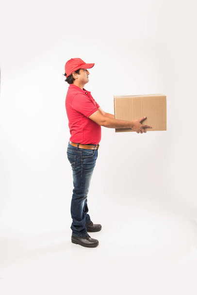 Delivery Concept - Portrait of Happy Indian or delivery man in red or green uniform walking or jumping or checking or presenting cardboard box with copy space - Photo, Image