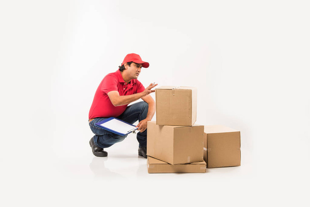 Delivery Concept - Portrait of Happy Indian or delivery man in red or green uniform walking or jumping or checking or presenting cardboard box with copy space - Foto, immagini