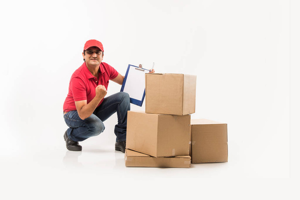 Delivery Concept - Portrait of Happy Indian or delivery man in red or green uniform walking or jumping or checking or presenting cardboard box with copy space - Foto, immagini