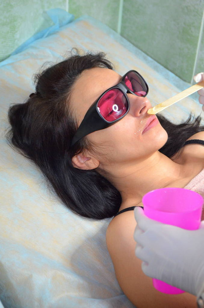 Laser-Haarentfernung. Haarentfernung über der Oberlippe. ein Mädchen mit Brille in einem Schönheitssalon - Foto, Bild