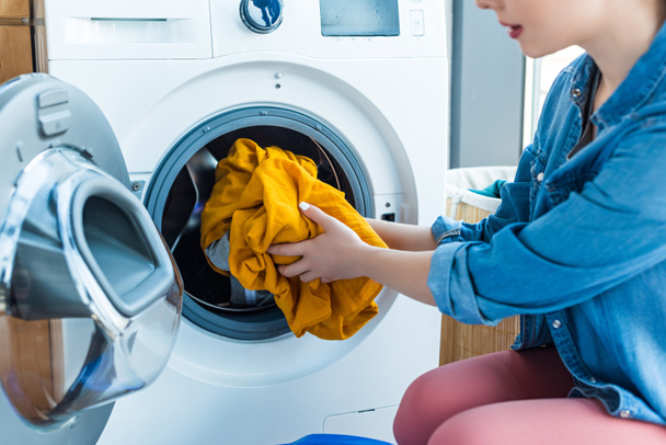 обрезанный снимок молодой женщины, кладущей белье в стиральную машину
 - Фото, изображение