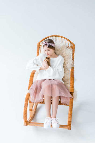 beautiful girl holding furry rabbit while sitting on rocking chair isolated on white  - Photo, Image