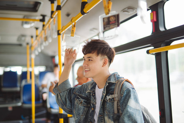 Asian man taking public transport, standing inside bus. - Foto, afbeelding