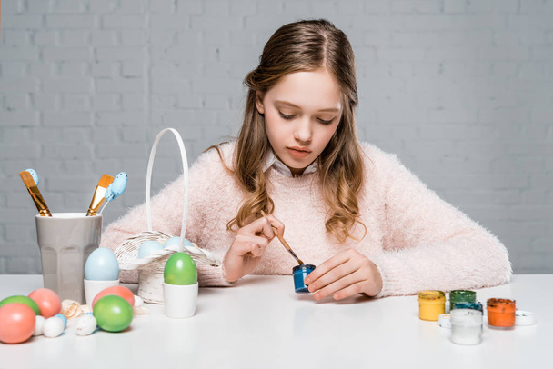 красива маленька дівчинка малює великодні яйця за столом
  - Фото, зображення
