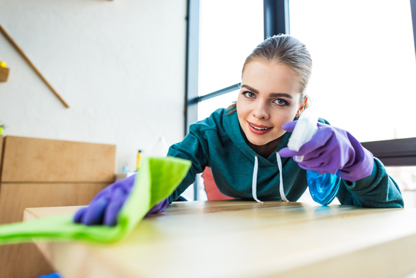 young woman smiling at camera while cleaning home with rag  - Photo, Image