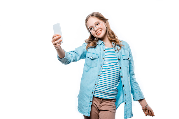 cute smiling teenage girl in eyeglasses taking selfie with smartphone isolated on white - Foto, Imagem