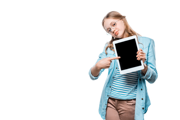 χαμογελώντας εφηβικό κορίτσι κρατώντας ψηφιακή δισκίο και δείχνοντας με το δάχτυλο στο κενή οθόνη που απομονώνονται σε λευκό  - Φωτογραφία, εικόνα