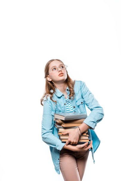 cute teenage girl in eyeglasses holding stack of books and looking up isolated on white - Fotoğraf, Görsel