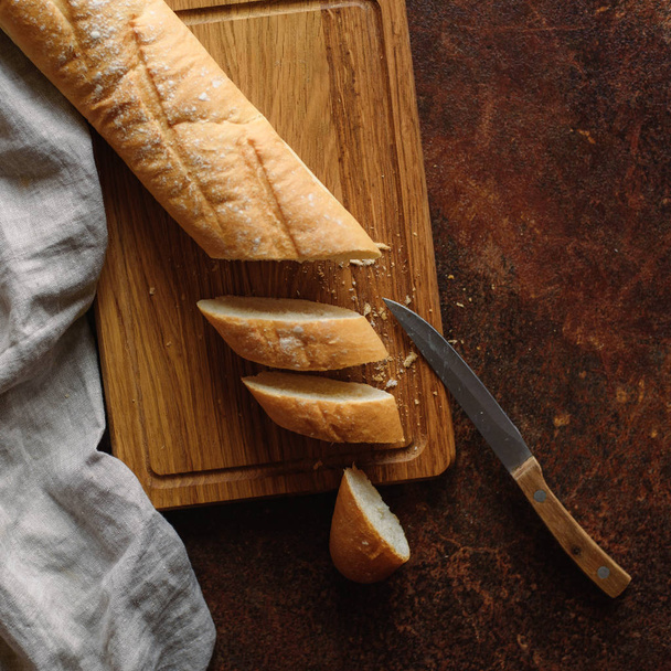 View of sliced baguette with knife on wooden chopping board  - Foto, immagini