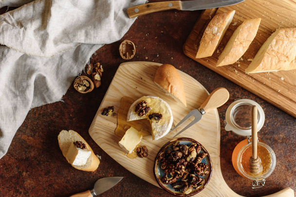 View of appetizing meal with honey jar,  brie, walnuts and sliced baguette. - Foto, Imagem