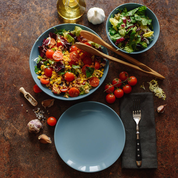 Vista superior da salada vegetariana com milho, tomate cereja, alface, repolho e salsa com molho picante na mesa de madeira
. - Foto, Imagem