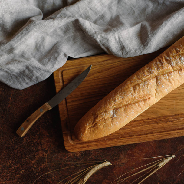 Top view of  baguette served on wooden chopping board with knife and napkin - Foto, immagini