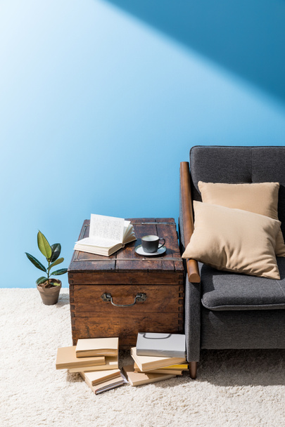 viejo cofre de madera con taza de café y libros cerca de sofá en frente de la pared azul
 - Foto, Imagen