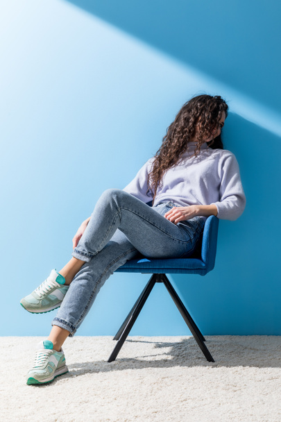 приваблива молода жінка сидить у кріслі перед синьою стіною
 - Фото, зображення