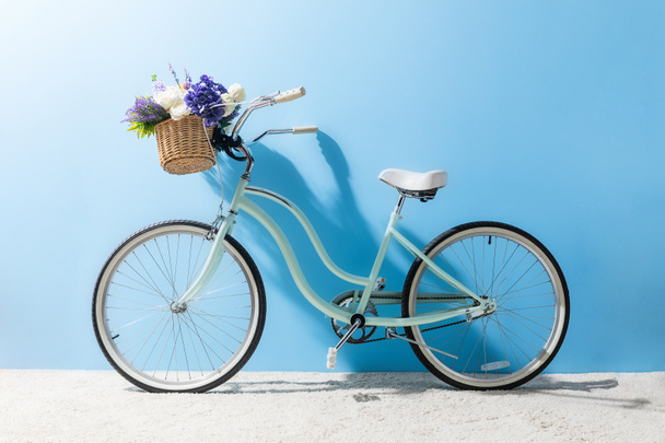 vista lateral de la bicicleta con flores en cesta delante de la pared azul
 - Foto, Imagen