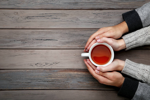 Female and male hand holding cup of tea on wooden table - Foto, Imagem