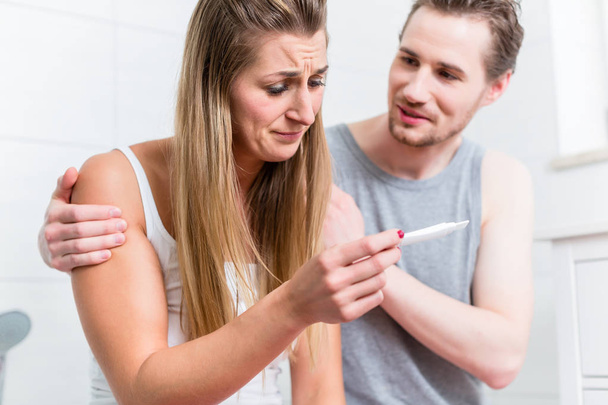 Mladá žena je smutné o výsledku těhotenského testu a její manžel, uklidňující a objal ji  - Fotografie, Obrázek