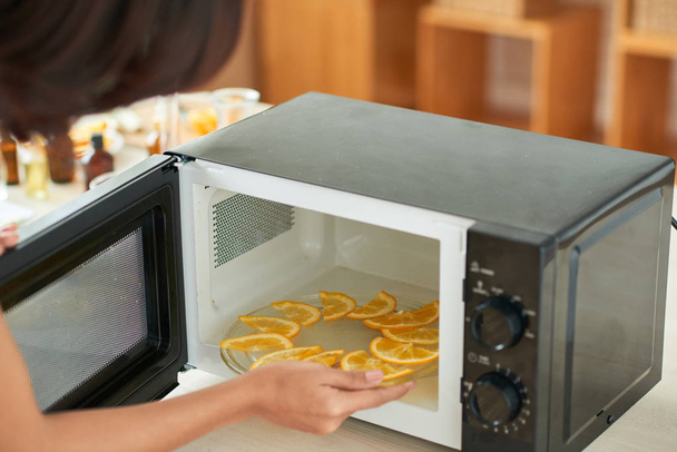 Frau legt Teller mit geschnittener Orange zum Trocknen in die Mikrowelle - Foto, Bild