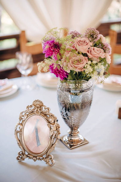 Tischnummer in silbernem Rahmen mit Ziffer, Blumenstrauß in Metallvase auf Hintergrund - Foto, Bild