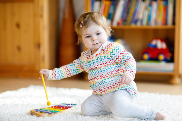 Adorable linda y hermosa niña jugando con juguetes educativos de música de madera en casa o en el vivero. Niño pequeño con xilofón colorido
 - Foto, imagen