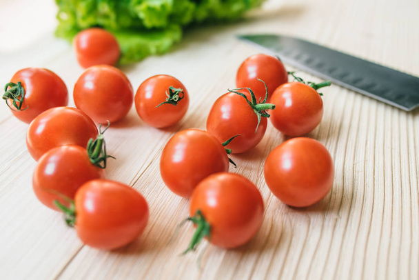 Ripe tomatoes and green lettuce on a wooden table with kitchen knife at the background. - Foto, Bild