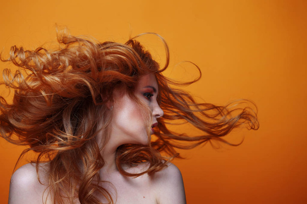 Beautiful redheaded girl with luxurious curly hair. Studio portrait on yellow background. Excellent hair - Foto, imagen