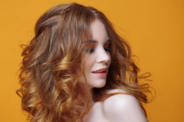 Happy redheaded young woman with luxurious curly hair. Studio portrait on yellow background. Excellent hair - Foto, Bild