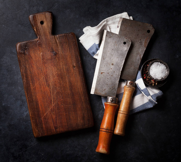 Carnicero. Cuchillos de carne vintage, especias y tabla de cortar sobre tabla de piedra. Vista superior con espacio
  - Foto, Imagen
