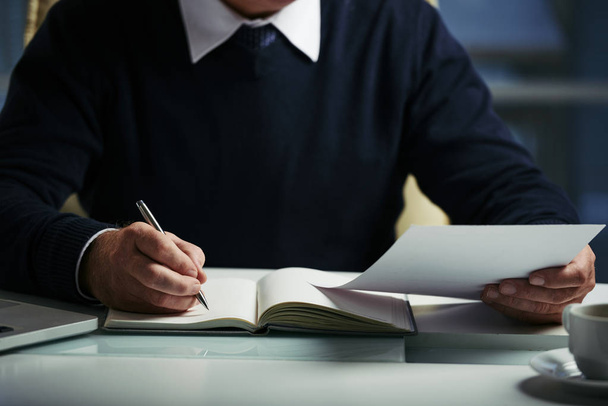 Обрізане зображення бізнесмена, який читає документи та робить нотатки
 - Фото, зображення